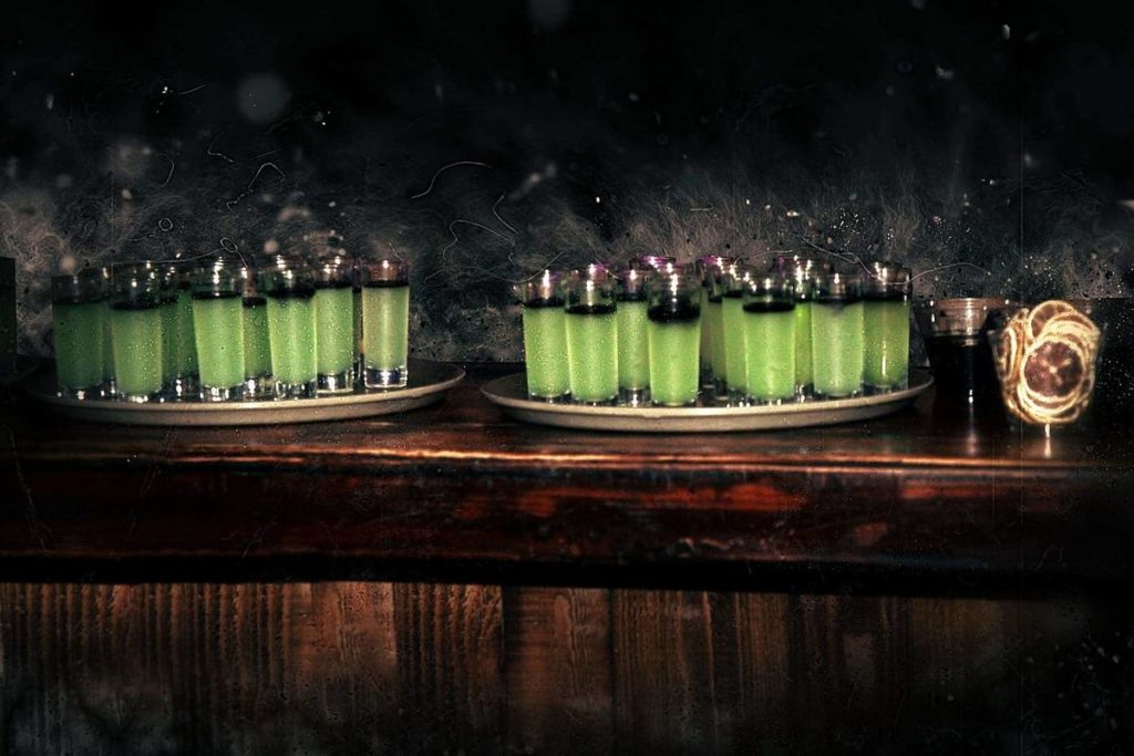 a round of green shots on a tray on a bar at the haunted tavern experience in a dark setting