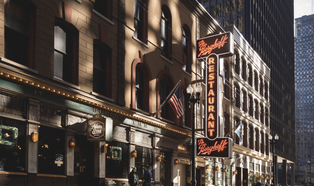 A light up red sign saying Berghoff’s along a brick building with the american flag in chicago