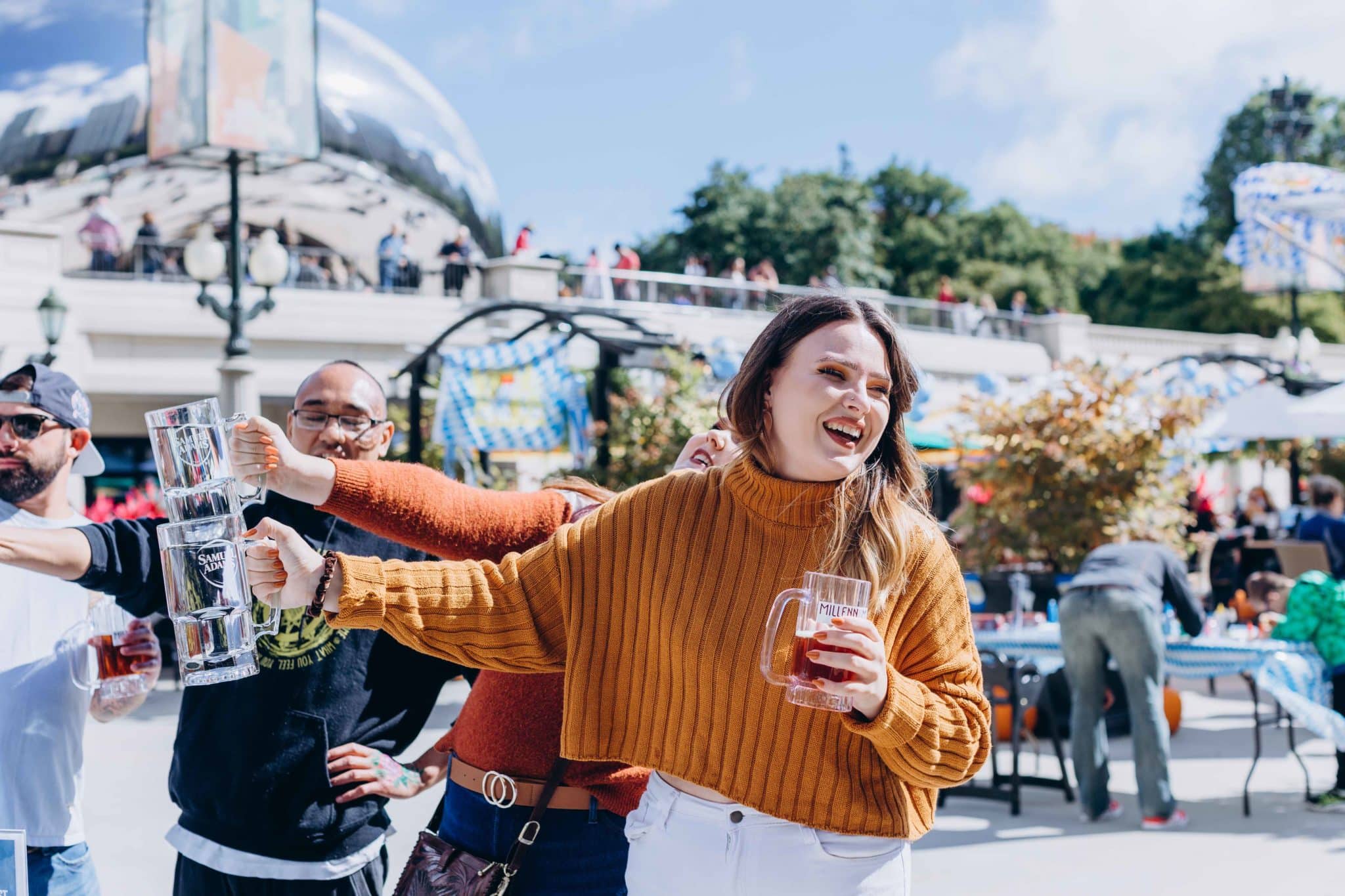 a woman in an orange sweater celebrating at Millenium Hall Oktoberfest saying Cheers with a beer in hand