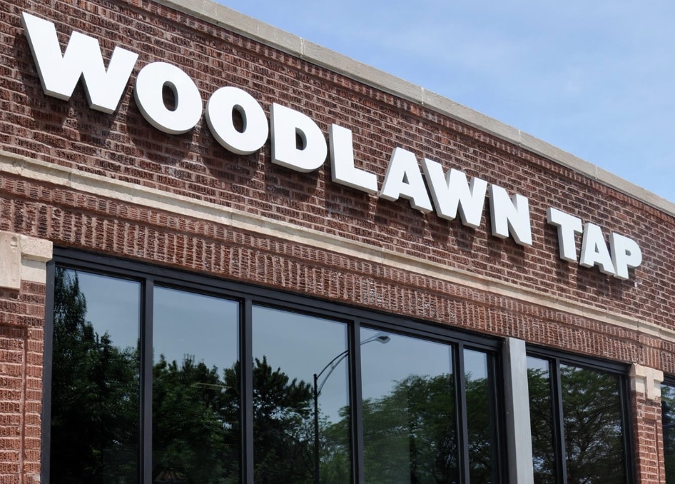 large white letters displaying the sign woodlawn tap on brickwall with a window underneath in chicago