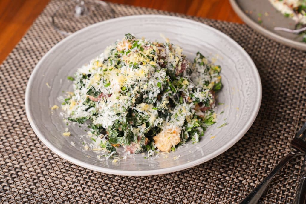 Tuscan Kale Salad with dressing and shaved parmesean on top on a white plate from florentine's thanksgiving dinner in chicago