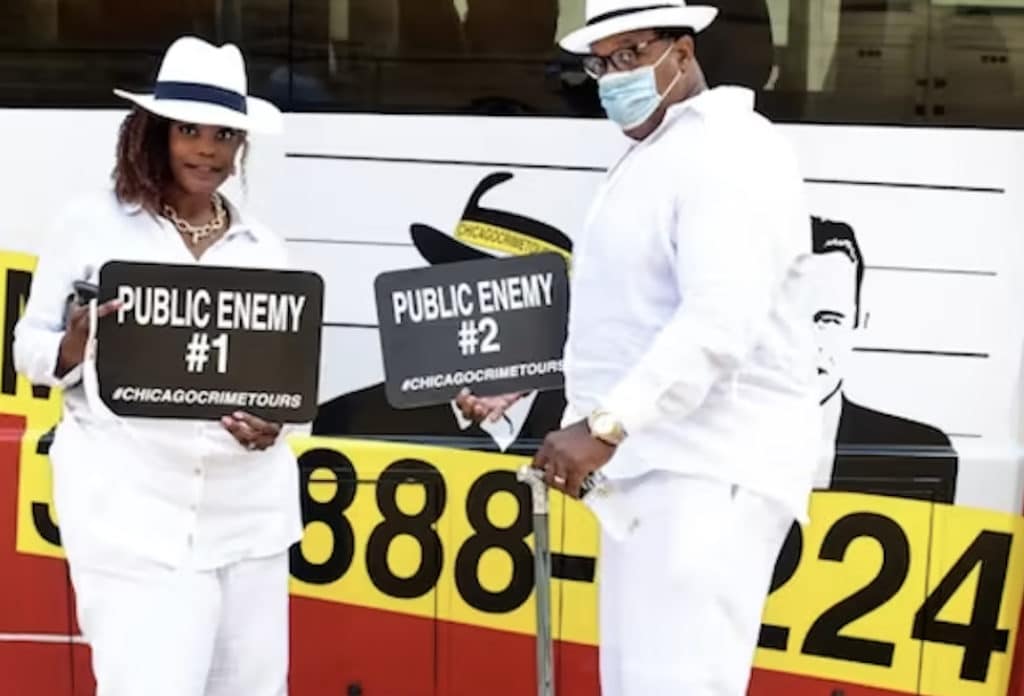 two people wearing a white suit holding public enemy signs in front of a bus