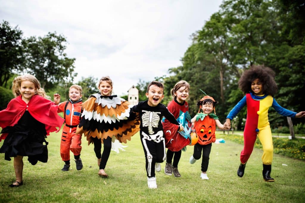 Little kids in a watch costume, skeleton costume, and a clown costume at a Halloween party