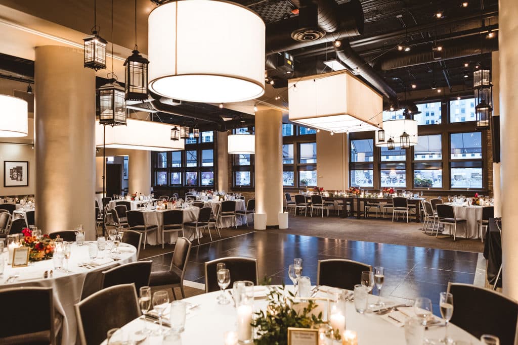 interior of river roast with light fixtures hanging from above and tables set with napkins and glasses with flower arrangements next to the Chicago river