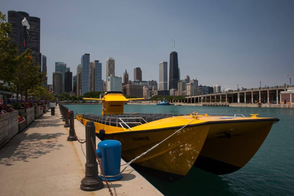 Horizontal sunny view of a yellow tourist catamaran, anchored in Navy Pier, with Chicago skyline in the background, including John Hancock Center
