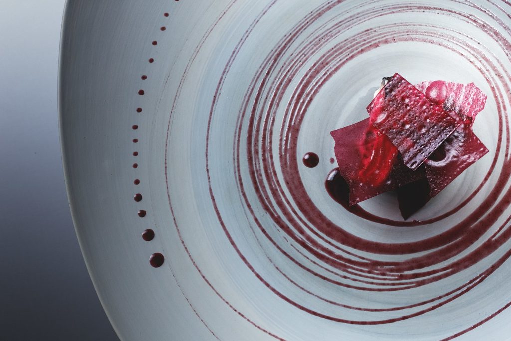 a red sauce dish surrounded by red droplets on a white plate from Alinea, a michelin-starred restaurant in Chicago